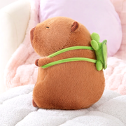 Side view of the Capybara Dreams plush backpack toy, showcasing the adorable green turtle design attached to its back, on a white surface.
